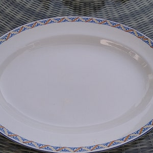 May include: A white oval serving platter with a blue and orange patterned border.