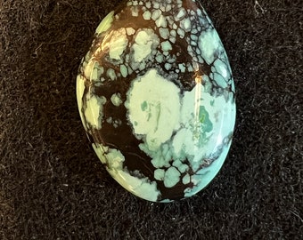 Può includere: Un cabochon di turchese liscio di forma ovale con una matrice marrone scuro e un colore blu chiaro e verde.
