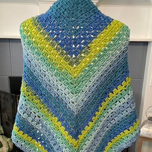 May include: A crocheted shawl in shades of blue and green. The shawl is made with a simple stitch pattern and has a triangular shape.