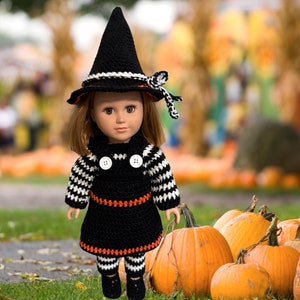 May include: A doll wearing a black and white witch costume with a black pointed hat and a black and orange dress. The doll is standing in front of a pile of pumpkins.