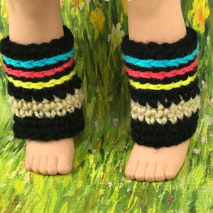 May include: A pair of black crochet leg warmers with colourful stripes and a tan crocheted trim. The leg warmers are on a doll's legs.