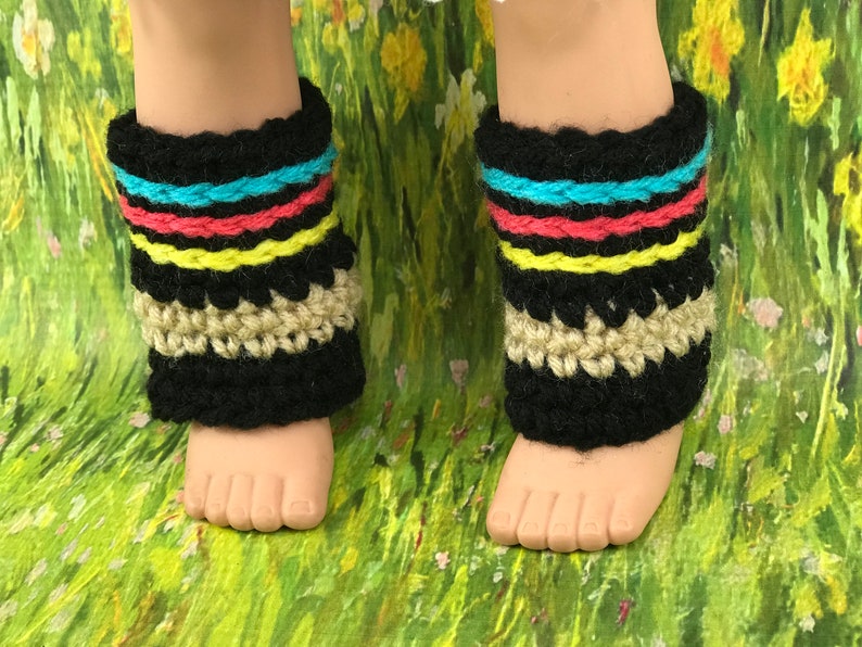 May include: A pair of black crochet leg warmers with colourful stripes and a tan crocheted trim. The leg warmers are on a doll's legs.