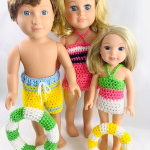 May include: Three dolls wearing crocheted swimwear and holding crocheted life preservers. The dolls have blonde hair and blue eyes. The swimwear is in shades of pink, green, yellow, and blue.