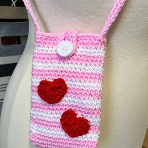 May include: A pink and white striped crocheted crossbody bag with a white button closure and two red crocheted hearts.