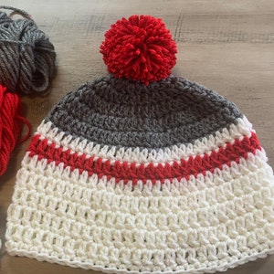 May include: A white, gray, and red crocheted hat with a red pom-pom on top.
