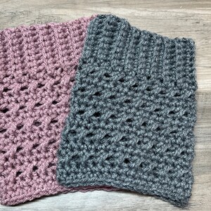 Op de afbeelding: Twee gehaakte vierkanten, een in een stoffige roze kleur en een in een donkergrijs. Beide vierkanten hebben een kant-achtig, opengewerkt patroon.