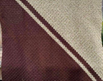 Peut inclure: Une couverture en crochet marron et beige avec un motif diagonal. La couverture est réalisée avec un point texturé et a une bordure en franges.