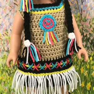 May include: A crocheted doll outfit in brown, black, white, yellow, pink, and blue. The outfit includes a dress with fringe, a hat, and leg warmers. The dress has a beaded design and a dreamcatcher motif.