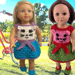 May include: Two dolls wearing crocheted cat-themed dresses. The doll on the left is wearing a purple, white, and blue dress. The doll on the right is wearing a pink, red, and green dress.