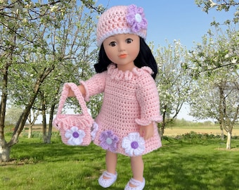 Puede incluir: Un vestido de crochet rosa con detalles de flores blancas y moradas. El vestido lo lleva una muñeca con el pelo negro y un sombrero de crochet rosa con una flor morada.