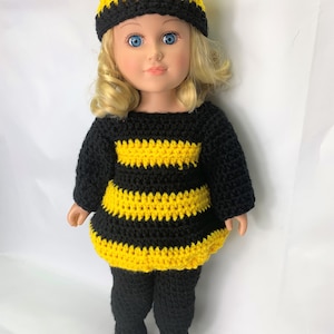 Puede incluir: Un disfraz de abeja de crochet para una muñeca, con un vestido a rayas amarillas y negras, pantalones a juego y un sombrero con forma de abeja con antenas.