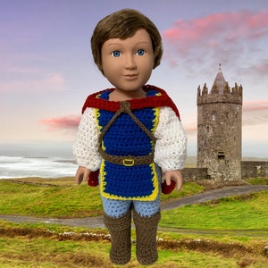 May include: A crocheted doll dressed as a prince, wearing a blue and yellow tunic, a red cape, and brown boots. The doll is standing in front of a stone tower.
