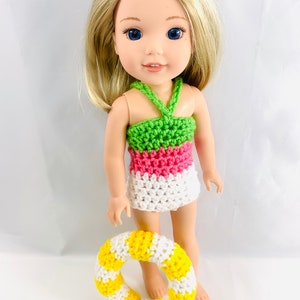 Puede incluir: Una muñeca rubia con un traje de baño de ganchillo verde, rosa y blanco y sosteniendo un salvavidas de ganchillo amarillo y blanco.
