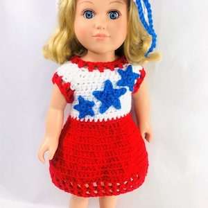 Op de afbeelding: Een pop die een rood, wit en blauw gebreid jurkje draagt met sterren en een bijpassende hoed. De pop heeft blond haar en blauwe ogen.