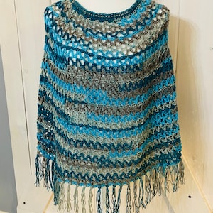 Könnte beinhalten: Ein gehäkeltes Poncho mit Fransenbordüre in den Farben Türkis, Blau und Braun.
