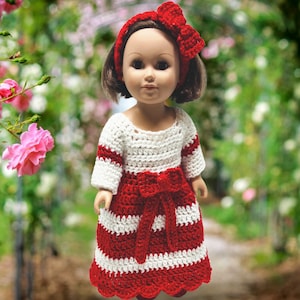 May include: A doll wearing a red and white striped crocheted dress with a red bow headband.