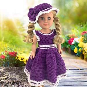 May include: A purple crochet dress with white trim and a matching white crochet hat with a purple flower accent. The doll is wearing the dress and hat.