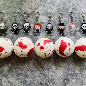 May include: A collection of horror-themed keychains featuring iconic characters like Jason, Ghostface, and Chucky, paired with white bath bombs splattered with red paint, creating a spooky aesthetic. The keychains have silver rings.