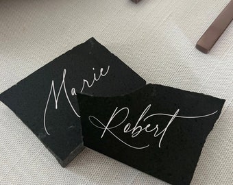 May include: Two black slate place cards with white calligraphy. The top card reads "Marie" and the bottom card reads "Robert".