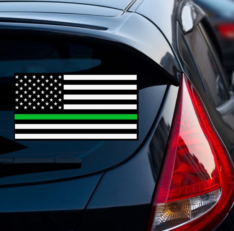 Puede incluir: Un coche negro con una calcoman&iacute;a de bandera estadounidense con una l&iacute;nea verde en la ventana trasera.