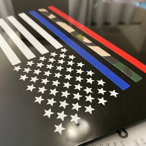 Puede incluir: Un fondo negro con un dise&ntilde;o de bandera estadounidense blanca. La bandera tiene una l&iacute;nea azul en el medio, una franja roja sobre la l&iacute;nea azul y un patr&oacute;n de camuflaje sobre la franja roja.