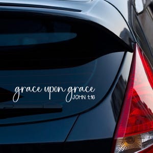 以下が含まれることがあります： 黒い車に「grace upon grace JOHN 1:16」という文字が書かれた白いビニールステッカー
