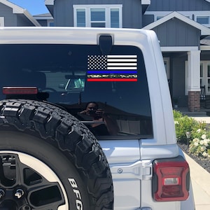 Puede incluir: Un Jeep blanco con una calcoman&iacute;a de bandera estadounidense de l&iacute;nea azul delgada en la ventana trasera. La calcoman&iacute;a tiene una l&iacute;nea roja delgada, una l&iacute;nea amarilla delgada y un patr&oacute;n de camuflaje.