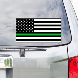 Puede incluir: Una bandera estadounidense en blanco y negro con una fina franja verde en el medio. La bandera est&aacute; en la ventana de un coche.