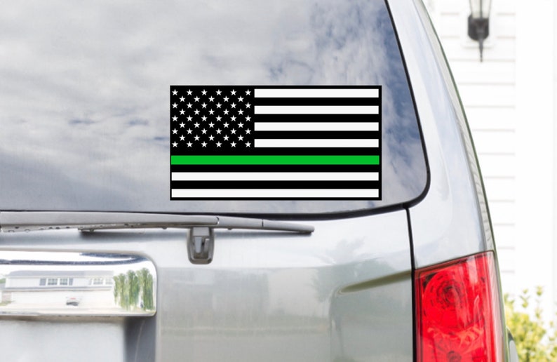 Puede incluir: Una bandera estadounidense en blanco y negro con una fina franja verde en el medio. La bandera est&aacute; en la ventana de un coche.