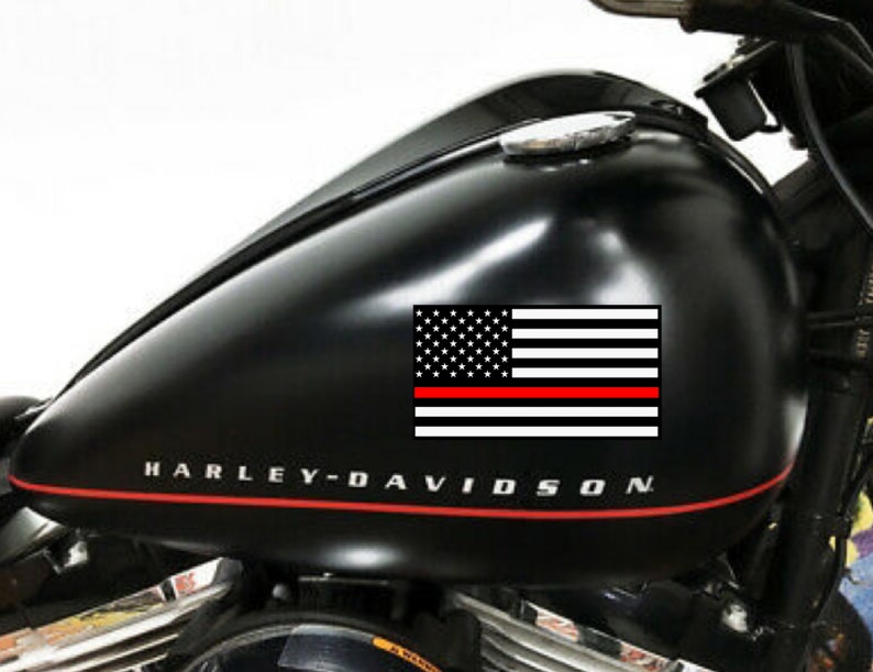May include: Black motorcycle gas tank with a red, white, and blue American flag decal with a red stripe across the bottom. The tank has the words "Harley-Davidson" printed on it.