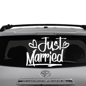 May include: A silver SUV with a black rear window. The rear window has a white vinyl decal that says "Just Married" with two hearts.