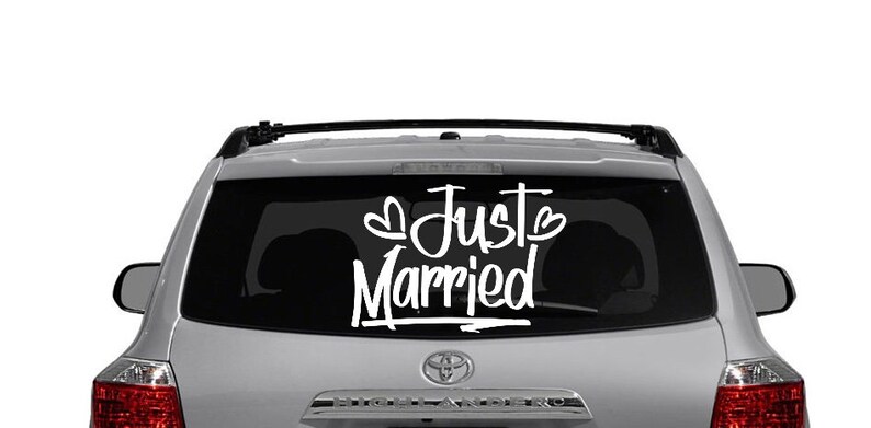 May include: A silver SUV with a black rear window. The rear window has a white vinyl decal that says "Just Married" with two hearts.