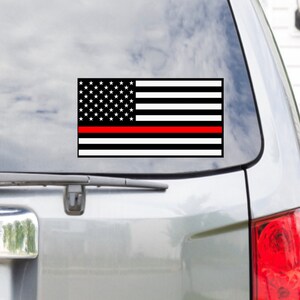 May include: A black and white American flag with a single red stripe across the middle. The flag is on a car window.