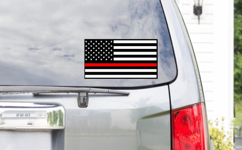 May include: A black and white American flag with a single red stripe across the middle. The flag is on a car window.