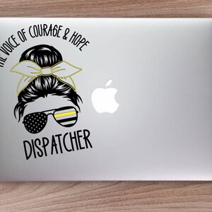 Puede incluir: Una ilustraci&oacute;n en blanco y negro de una mujer con un mo&ntilde;o desordenado y una cinta amarilla y negra. Lleva gafas de sol con una fina raya amarilla y un patr&oacute;n de bandera estadounidense. El texto "The Voice of Courage & Hope Dispatcher" est&aacute; debajo de la ilustraci&oacute;n.