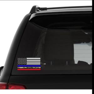 Puede incluir: Un coche negro con una calcoman&iacute;a de bandera estadounidense blanca, roja y azul en la ventana trasera. La bandera tiene una l&iacute;nea azul fina y una l&iacute;nea roja fina con un patr&oacute;n de camuflaje.