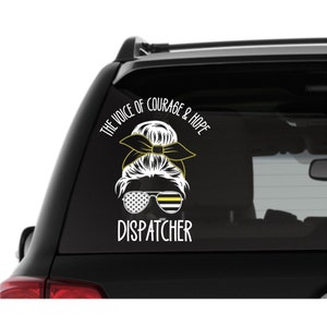 Puede incluir: Una calcoman&iacute;a de ventana de autom&oacute;vil blanca con un gr&aacute;fico negro y amarillo de una mujer con un mo&ntilde;o, gafas de sol y una cinta. El texto dice "The Voice of Courage & Hope Dispatcher".