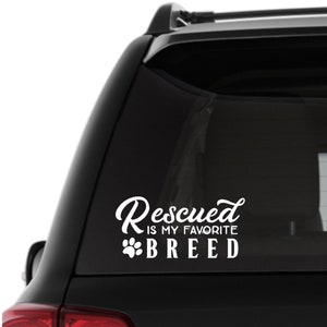 Puede incluir: Pegatina de coche de vinilo blanco con el texto "Rescued is my favorite breed" y una huella de pata.
