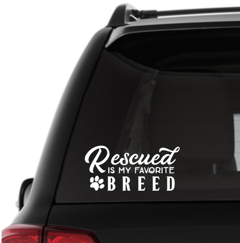 Puede incluir: Pegatina de coche de vinilo blanco con el texto "Rescued is my favorite breed" y una huella de pata.