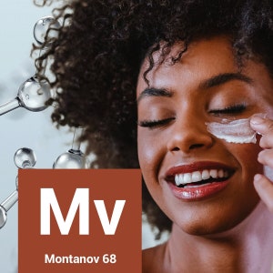 May include: A close-up of a woman's face with her eyes closed. She is smiling and has a white cream on her cheek. The image also includes a brown square with the text "Mv" and "Montanov 68" in white.