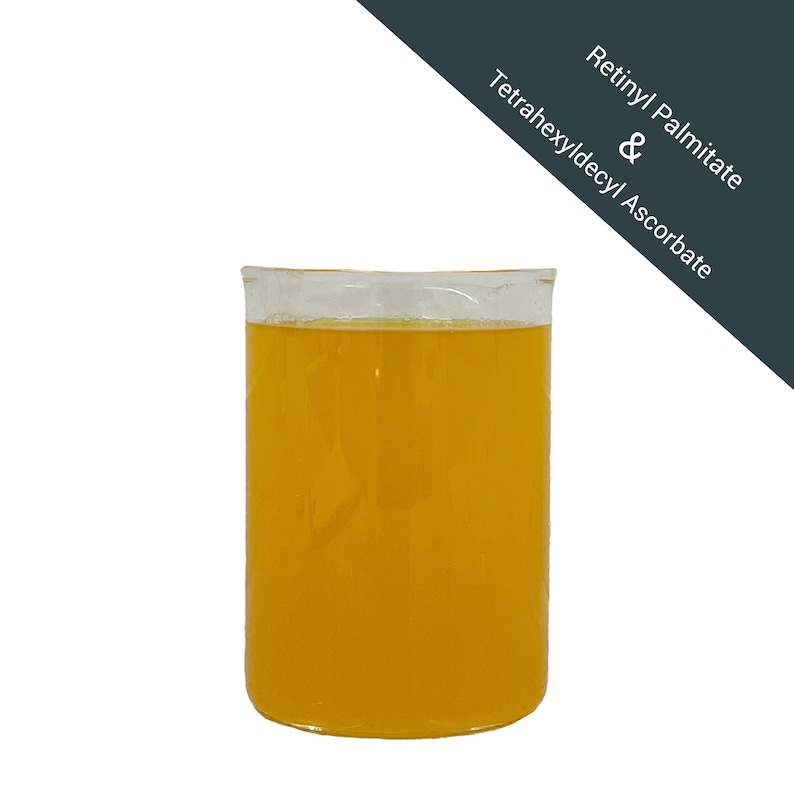 May include: A clear glass beaker filled with a bright yellow liquid. The text "Retinyl Palmitate & Tetrahexyldecyl Ascorbate" is written on a dark gray background.