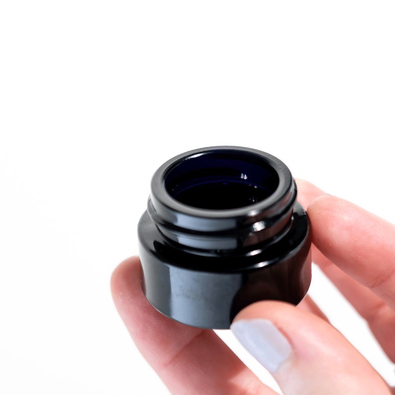 May include: A small, black glass jar with a blue interior. The jar is empty and has a smooth, shiny finish.