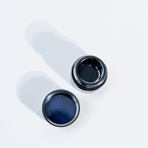 May include: Two round, silver-rimmed containers with dark blue lids. The lids are slightly indented in the center.