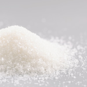 May include: A close-up of a pile of white granulated sugar on a gray surface.