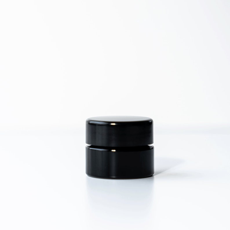 May include: A black cylindrical container with a lid. The container is made of a smooth, glossy material.