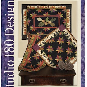 May include: A pattern booklet titled Masquerade, a companion for Studio 180 Design's Rapid Fire Hunter's Star - Petite Star Tool. The cover displays three quilted projects featuring black backgrounds, star motifs, pumpkins, and black cats.