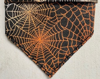 Könnte beinhalten: Schwarzes Stoffbandana mit einem weißen und orangefarbenen Spinnennetz-Muster.