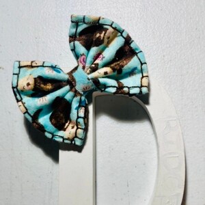 May include: White wooden letter D with a blue and brown bow tied to the top. The bow has a pattern of small brown animals on a light blue background.