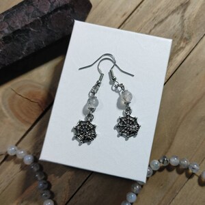 Puede incluir: Un par de pendientes de araña de plata con una cuenta de ágata blanca en cada pendiente.