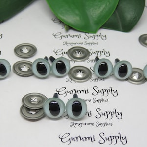 May include: A close-up of a set of 10 plastic safety eyes for amigurumi projects. The eyes are white with black pupils and have a silver metal washer and a plastic post for attaching to a project. The eyes are arranged in two rows on a white surface with the text "Gurumi Supply" printed on the surface.